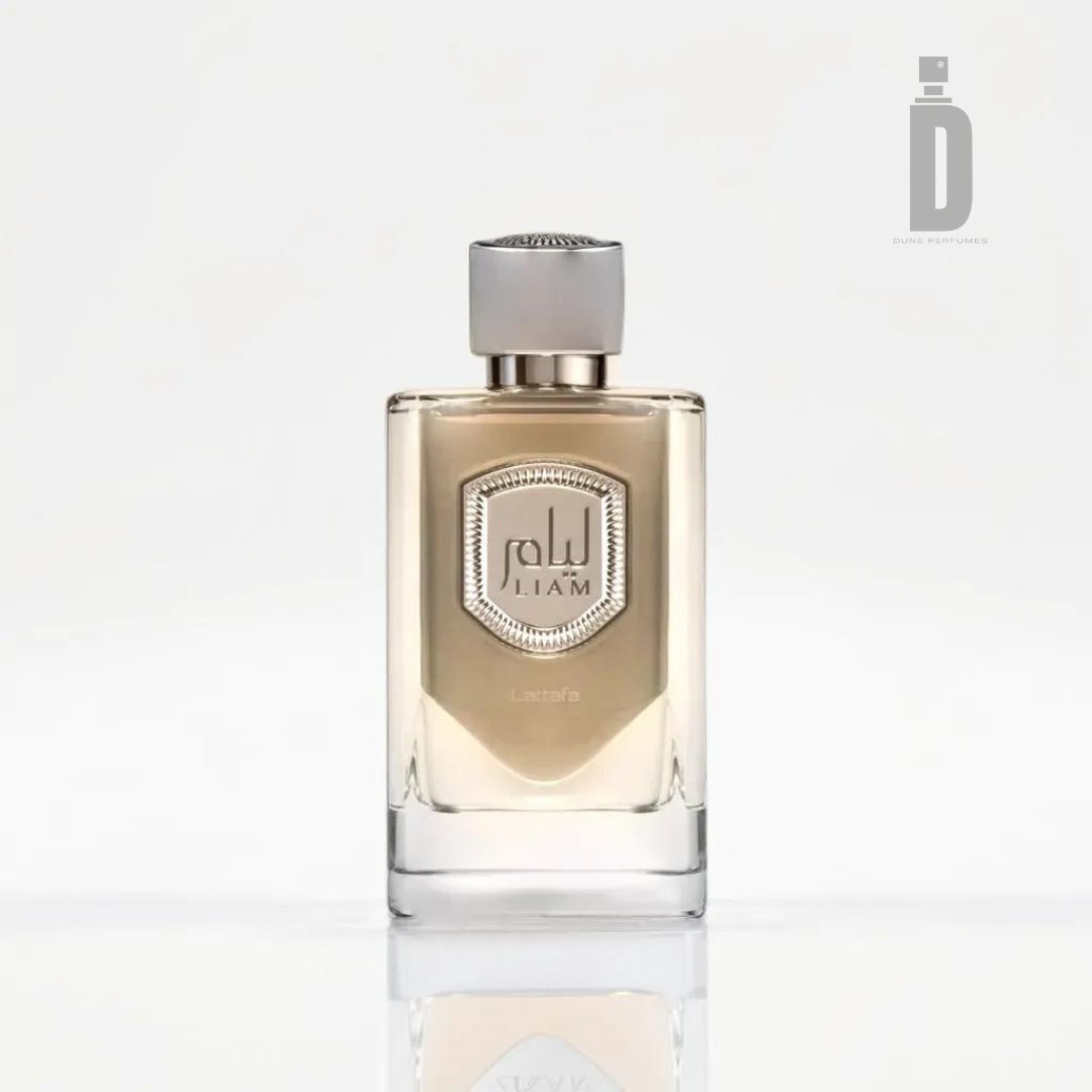 A clear glass perfume bottle with a silver cap, filled with a light-colored liquid. The label on the front displays Arabic text and the brand name "Lattafa." The background is white with the logo "D" for Dubai Fragrance in the top right corner, showcasing a sophisticated blend of refined allure. This exquisite presentation embodies the essence of Liam Grey 100ml EDP by Lattafa.