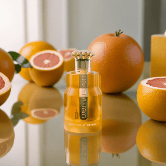 The Paris Corner LUEUR D’ESPOIR MEMORIES OF SUMMER 100ml EDP sits on a reflective surface, surrounded by fresh grapefruits, oranges, and bergamot, as soft natural light highlights this vibrant summer fragrance.