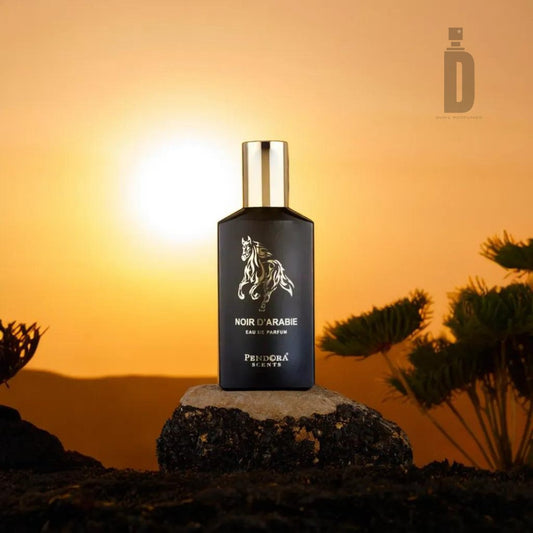 A black bottle of "Noir D'Arabie Pendora 100ml Eau de Parfum" by Paris Corner, embodying Arabian allure, is displayed against a backdrop of a golden sunset. The bottle features a silver cap and a horse emblem. Surrounding it are silhouetted trees and rocks, with a soft glow highlighting the scene.