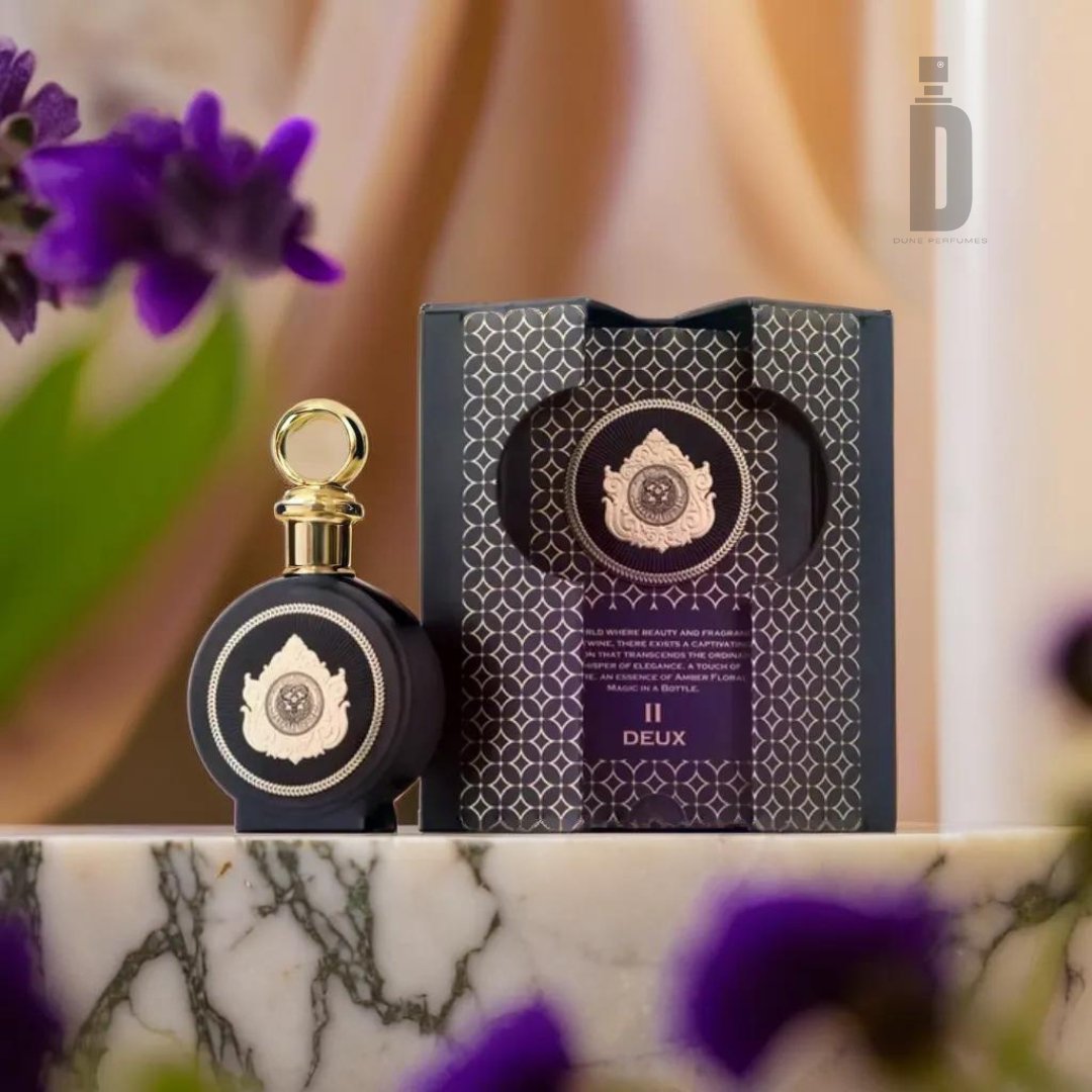 A luxurious perfume bottle with a gold cap sits in front of a decorative box labeled "North Stag Expressions 2 Deux 100ml EDP" by Paris Corner. The background features purple flowers and a marble surface, creating an elegant and sophisticated setting for this refined fragrance.