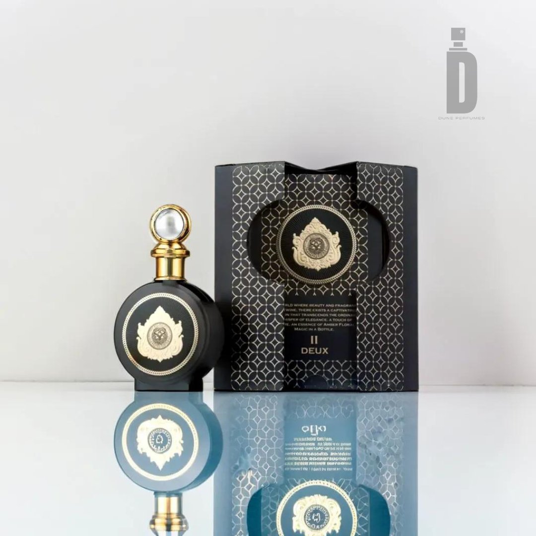 A luxurious black perfume bottle with gold accents stands next to its matching black and gold patterned box, branded as Paris Corner's North Stag Expressions 2 Deux 100ml EDP. The bottle features a circular emblem on the front and a crystal-topped cap, exuding an elegant and adventurous vibe. Both the box and bottle are reflected on a glossy surface below.