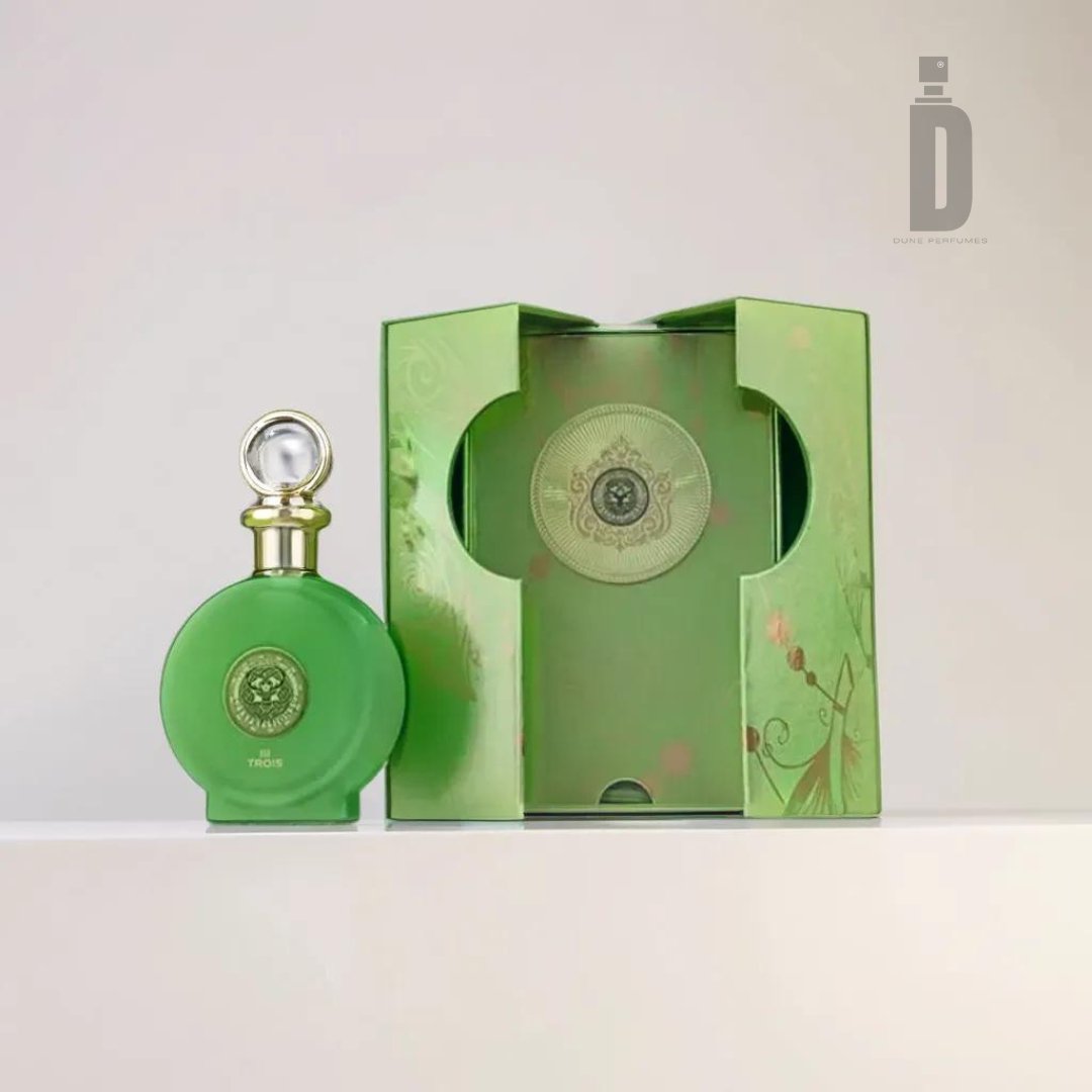 A green glass perfume bottle with a round shape and a gold emblem, containing the sophisticated fragrance of North Stag Expressions 3 Trois 100ml EDP by Paris Corner, is displayed next to its matching green box. The box features artistic floral designs and a cutout that showcases the bottle inside. The partially open box reveals the luxurious packaging.