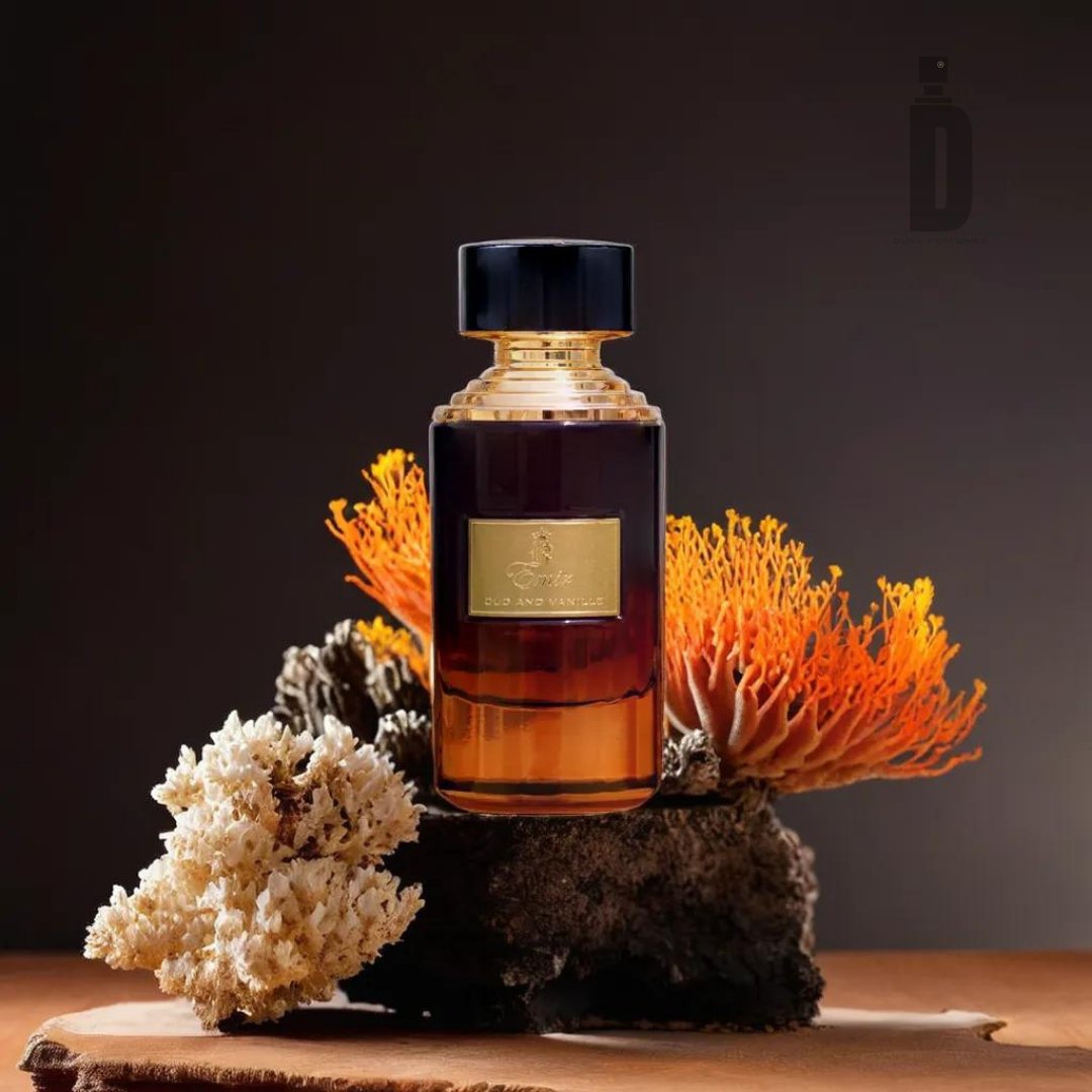 The Oud and Vanille 75ml EDP by Paris Corner features a dark amber bottle with a black cap and a golden label, elegantly poised on a piece of natural coral against a dark background. The hint of Oud and Vanille adds depth, while the orange coral accents bring a vibrant touch to the sophisticated display.