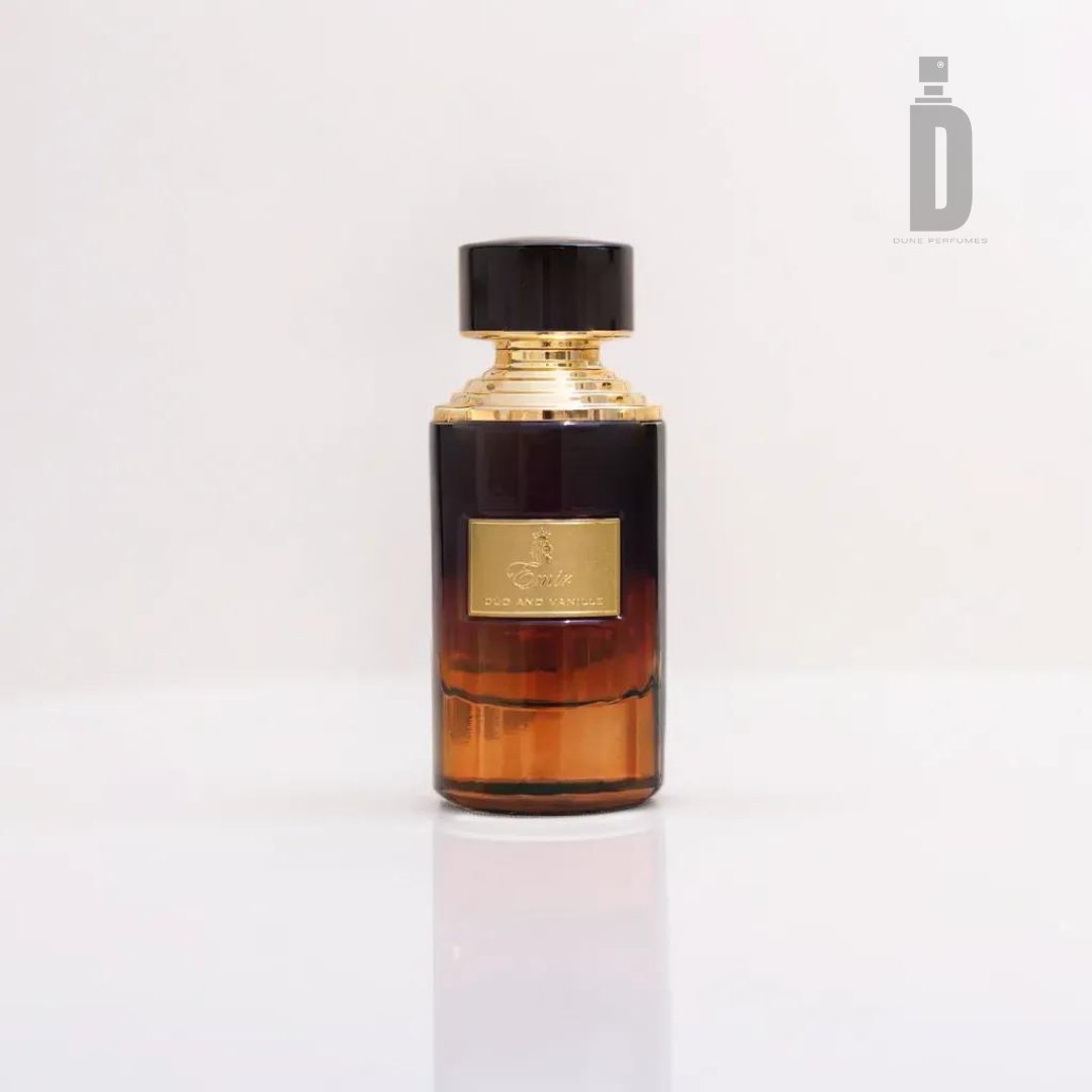 A sleek glass bottle of Paris Corner's Oud and Vanille 75ml EDP - Emir rests on a white background. The bottle showcases a gradient design, transitioning from black at the top to amber at the bottom, and is crowned with an elegant black and gold cap. A gold emblem and label adorn the front, hinting at the rich notes of Oud and Madagascar vanilla within.