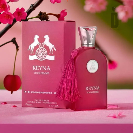 A pink perfume bottle labeled "Reyna 100ml EDP - Maison Al Hambra" sits beside its matching pink box decorated with white horse graphics. The bottle has a shiny silver cap and a pink tassel, exuding regal grace. Pink flowers and a cherry add a decorative flair in the background, enhancing the enchanting aroma of the Maison Al Hambra fragrance.