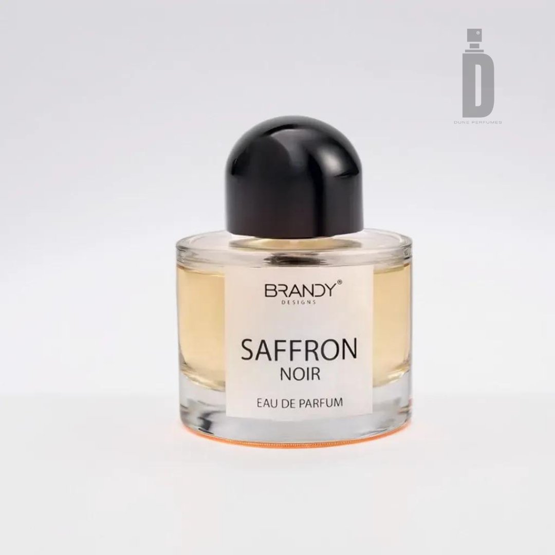 A clear glass bottle of luxury perfume labeled "BRANDY DESIGNS" and "Saffron 100ml EDP - Brandy Designs" with a black round cap. The bottle contains a yellowish liquid, exuding a captivating aroma, set against a plain white background.
