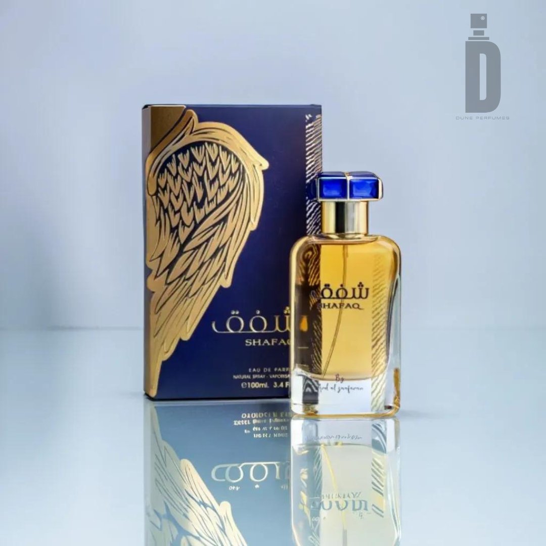 A gold-capped bottle of Shafaq 100ml EDP by Ard Al Zaafaran is placed in front of an ornate box adorned with a golden wing design. The perfume bottle and box are reflected on the glossy surface they sit on, exuding an exotic allure. The logo "D" of "Dubai Parfumerie" is in the top right corner.