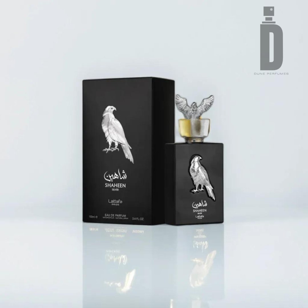 A dark bottle of Shaheen Silver 100ml EDP - Lattafa Pride by Lattafa, adorned with an engraved falcon and accompanied by its matching box featuring the same falcon illustration. The bottle boasts a sculpted falcon perched as the cap, with the Dune Perfumes logo visible in the upper right corner, emphasizing this exquisite fragrance.