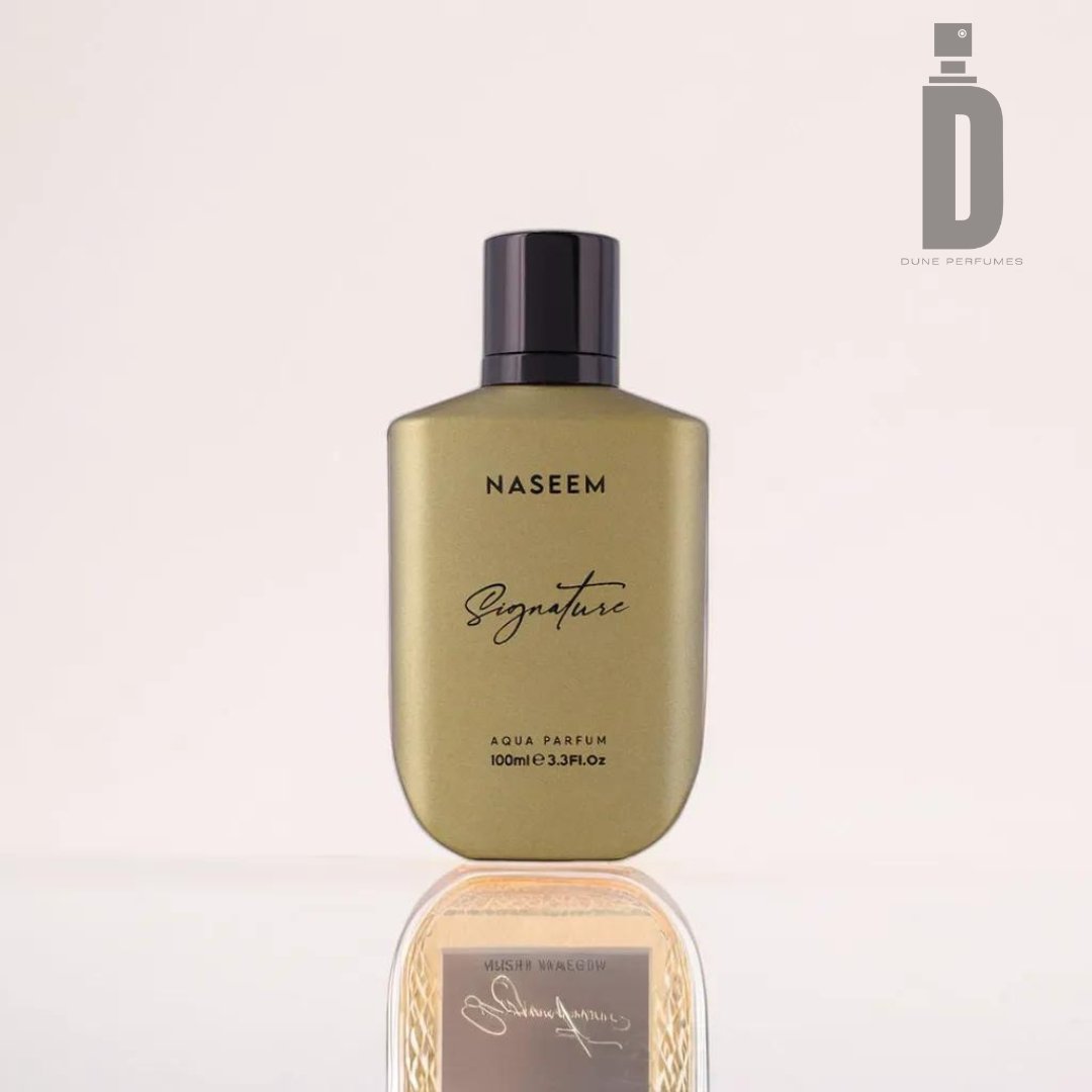 A sleek, gold-colored perfume bottle labeled "Signature Golden 100ml Aqua Parfum - Naseem (alcohol-free)" from Naseem Perfumes sits on a reflective surface. It features a modern design with a black cap, exuding luxury. The "Dune Perfumes" logo is visible in the top-right corner.