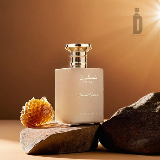 A square beige perfume bottle with a gold cap labeled "Taskeen Caramel Cascade 100ml EDP - Paris Corner," featuring Arabic text, is elegantly displayed among rocks and honeycomb on a soft brown background. Warm light from the top left highlights the luxurious fragrance. A minimalist "D" logo is positioned in the top right corner.