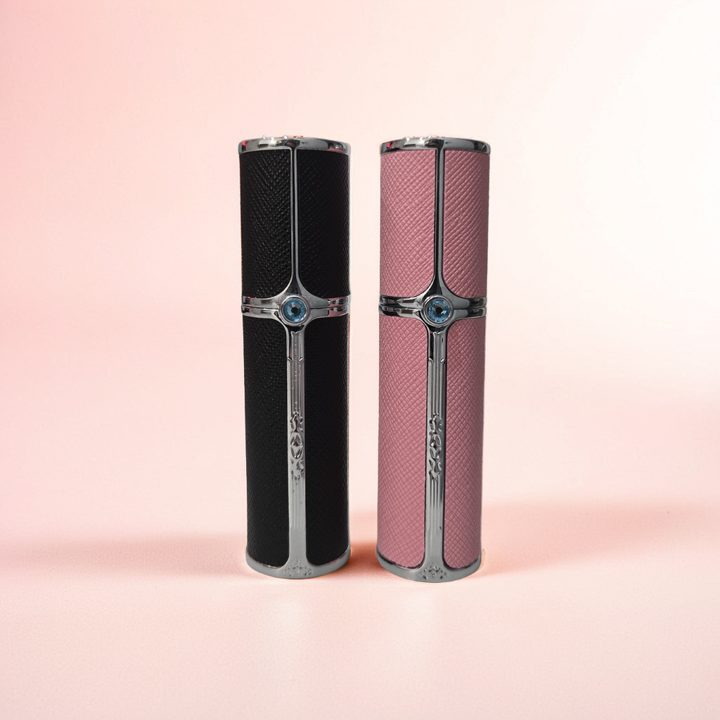 Dune Perfumes' 5ml & 10ml Travel Sprays sit on a soft pink surface with a gradient background. The cylindrical bottles, one black, one pink, are refillable, perfect for travel spray enthusiasts. Both feature metallic accents and a cross-like design.