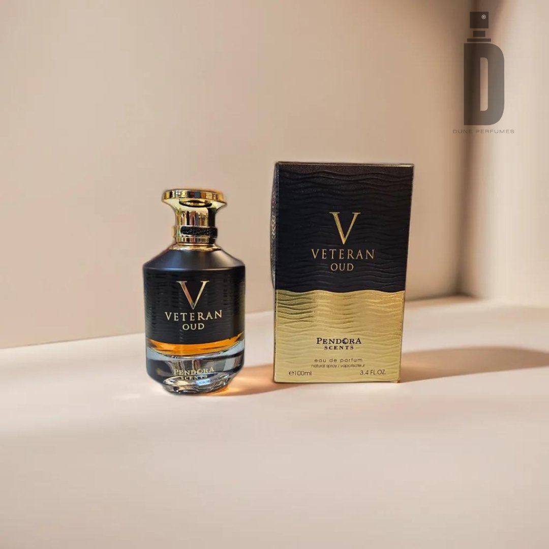 A bottle of Veteran Oud Pendora 100ml EDP by Paris Corner stands beside its matching box. The luxurious fragrance bottle transitions from a black base to a golden top, complemented by a shiny gold cap. The label reads "Veteran Oud." The box, featuring a similar black-to-gold design, is placed against a light background.