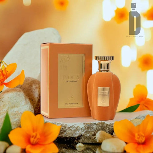 A bottle of Voux Patisserie 100ml Eau de Parfum from Paris Corner, a gourmand fragrance evoking the essence of a French patisserie, sits beside its matching box. The bottle and box are a warm orange color with gold accents. Bright orange flowers and soft, out-of-focus lights create a warm, inviting ambiance.