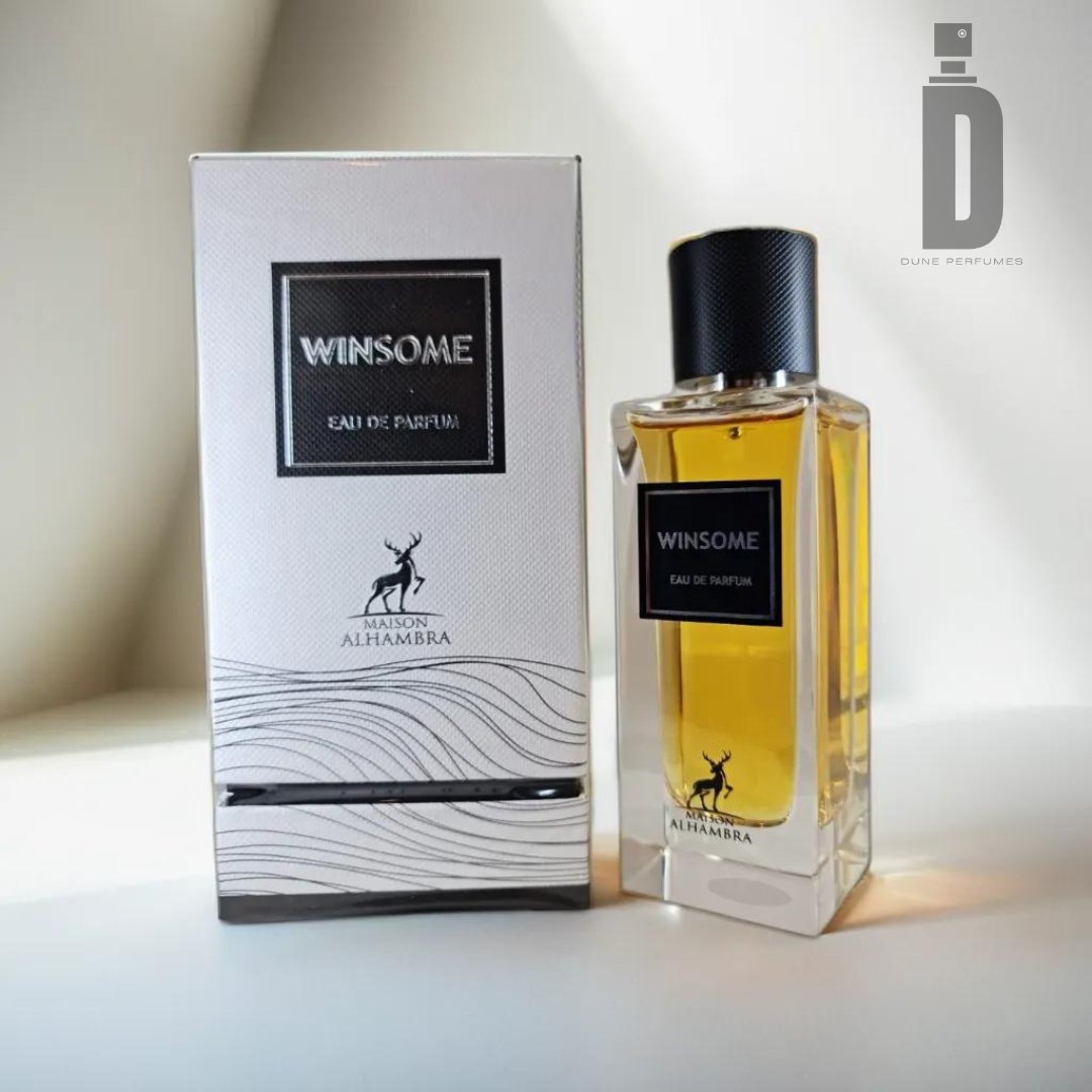 A rectangular bottle of Winsome (The Tux) 90ml Eau De Parfum stands next to its matching box. Both the bottle and the box, by Maison Alhambra, are adorned with a minimalist black and white design featuring a deer logo and the text "ALHAMBRA." The light brown liquid inside exudes a sophisticated blend that offers an irresistible allure.